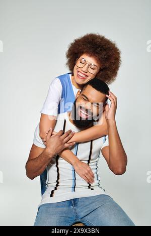 Un homme afro-américain dans des vêtements élégants porte une femme sur son dos sur un fond gris, montrant l'amitié. Banque D'Images