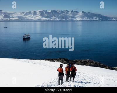 Touristes descendant une pente de neige à Palaver point, deux Hummock Island avec le navire de croisière Ocean Nova ancré dans la baie, Antarctique Banque D'Images