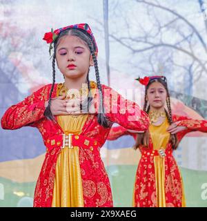 Almaty, Kazakhstan - 21 mars 2024 : deux petites filles asiatiques mignonnes dans des vêtements lumineux traditionnels nationaux dansant la danse tadjike sur scène pendant la célébration Banque D'Images