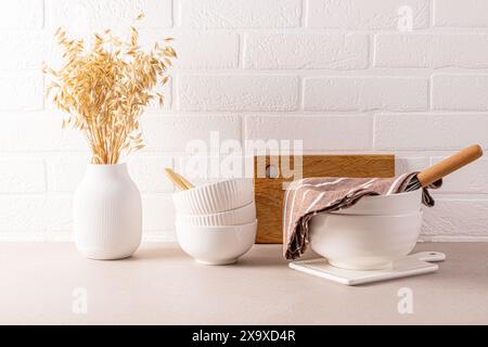 Ensemble de bols en céramique élégants blancs pour la cuisson, vase en gypse blanc avec des oreilles de blé sur le comptoir de cuisine. Mur de briques blanches. Cuisine écologique Banque D'Images