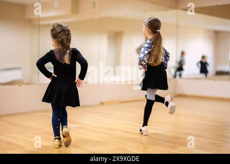 Deux jeunes filles pratiquant des mouvements de danse dans un studio de danse avec des miroirs. Ils portent des vêtements de danse et se concentrent sur leur reflet. Banque D'Images