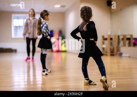 Deux jeunes filles pratiquant des mouvements de danse dans un studio lumineux tout en étant instruites par un professeur. L'atmosphère est concentrée et énergique. Banque D'Images