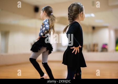 Deux jeunes filles pratiquant la danse dans une salle de classe avec des miroirs et un plancher de bois franc, portant des vêtements de danse et se concentrant sur leurs mouvements. Banque D'Images