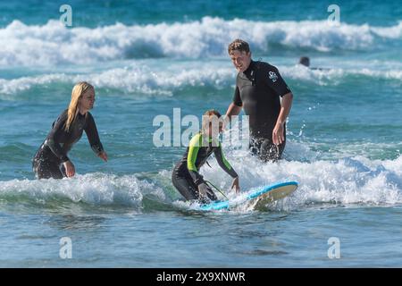 Une mère et un père aident leur jeune fille à apprendre à surfer à Fistral à Newquay en Cornouailles au Royaume-Uni. Banque D'Images