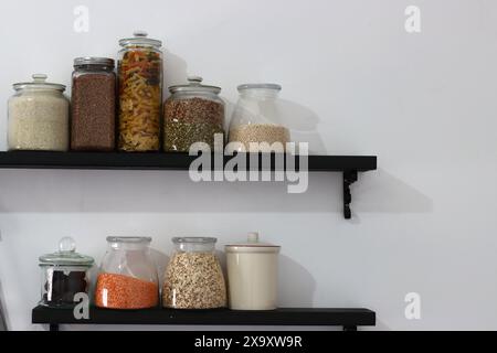 Garde-manger de cuisine approvisionné. Étagères avec différentes céréales dans des pots sur fond de mur blanc avec espace pour le texte. Différentes graines et céréales en verre Banque D'Images