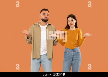 Homme et femme confus debout sur fond orange pendant la journée Banque D'Images
