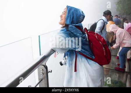 Voyageuse thaïlandaise visite pose portrait prendre une photo sur Glass Walkway ou Canyon Skywalk falaise abrupte dans le parc forestier national de Tianmen sous la pluie Banque D'Images