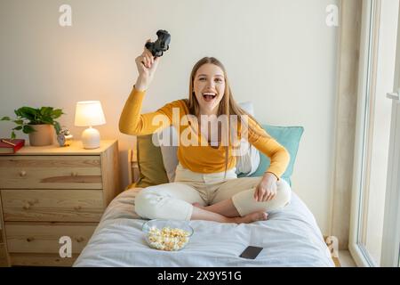 Fille jouant à des jeux vidéo sur le lit dans la chambre pendant la journée Banque D'Images