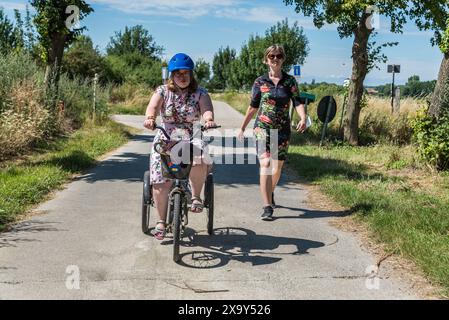 Jeune femme trisomique sur un tricycle et son amie en robe conduisant dans les champs de la campagne belge. Hakendover, Belgique, mod Banque D'Images