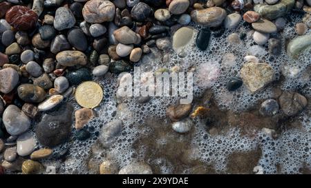 Pièce Bitcoin dorée placée sur un fond de grandes pierres grises le long de la côte, symbolisant la stabilité contemporaine de la monnaie électronique. Banque D'Images
