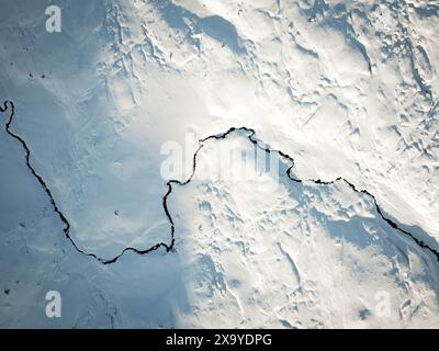 Une vue aérienne d'un petit ruisseau serpente à travers la couverture fraîche de neige. Banque D'Images