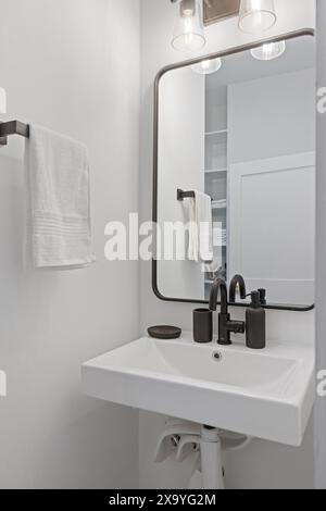 Salle de bains avec luminaires blancs, meuble-lavabo en bois sombre, serviette noire Banque D'Images