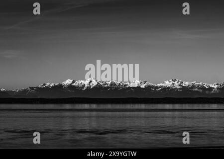 Un cliché monochrome de montagnes enneigées reflété dans un plan d'eau tranquille. Banque D'Images