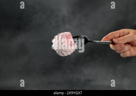 Délicates guimauves roses brochées sur une fourchette, placées sur un fond noir élégant. Cette image captivante ajoute une touche de douceur et d'élégance à Banque D'Images