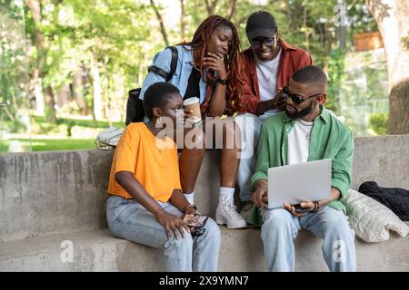 Amis satisfaits heureux camarades de classe étudiant avec un ordinateur portable assis sur le campus Banque D'Images