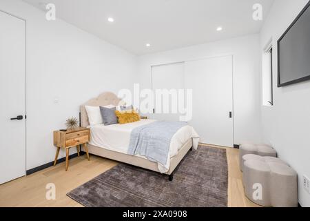 Une chambre bien rangée avec parquet et une grande télévision à écran plat montée au-dessus du lit Banque D'Images