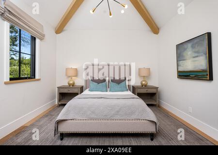 Chambre principale avec poutres apparentes, lit gris et murs blancs Banque D'Images