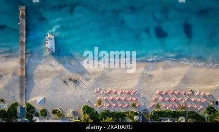 Planant au-dessus de la station balnéaire sur Grace Bay dans les îles Turques et Caïques. Les parapluies roses uniques et le quai brillent au coucher du soleil. Banque D'Images