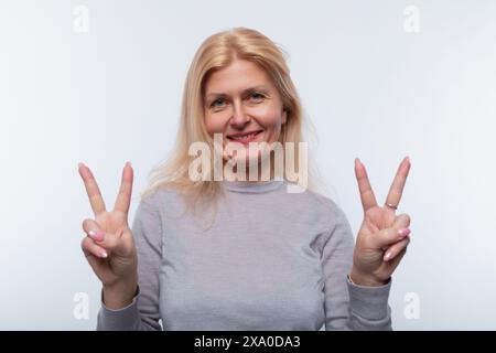 Charmante femme de 45 ans aux cheveux blonds montre un geste de convivialité Banque D'Images