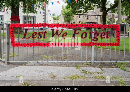 'Lest We Forget' avec des coquelicots tricotés fabriqués par des dames locales de long Preston. Sur l'affichage du village 3/6/24 avec d'autres grands groupes de coquelicots tricotés . Banque D'Images