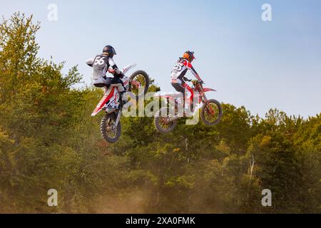 Deux motards de motocross planant au-dessus des arbres sur une piste de terre Banque D'Images