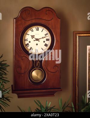 Horloge murale en bois vintage avec pendule et chiffres romains, montre antique classique montée sur le mur intérieur avec un éclairage chaleureux et un décor Banque D'Images
