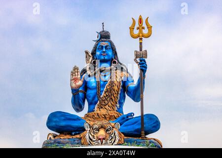 Statue bleue du Seigneur Shiva assise avec une peau de tigre, tenant un trident et affichant un geste de bénédiction. Orné de serpents et de perles, ce vibrant Banque D'Images