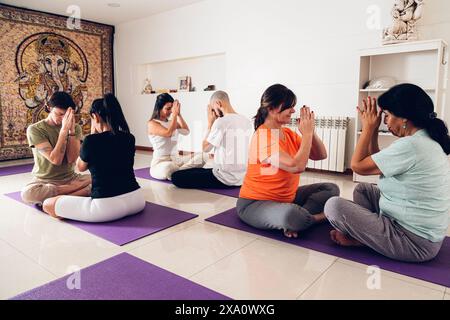 Les gens dans un cours de yoga. Ils font la position de prière avec leurs mains levées tout en étant assis sur un tapis dans le gymnase. Banque D'Images