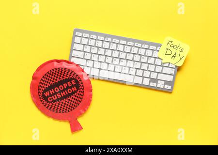 Clavier d'ordinateur, note collante et coussin whoopee sur fond jaune. Farce du jour des fous d'avril Banque D'Images