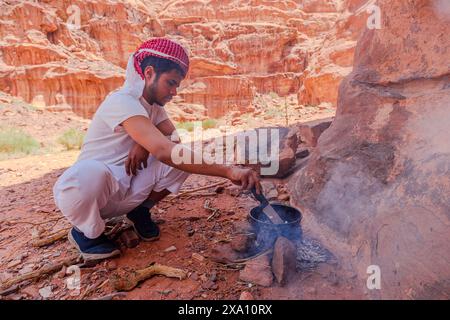 Jordanie - 1er mai 2024 : L'homme bédouin prépare un repas au-dessus d'un simple foyer de pierre au milieu des sables rouges emblématiques du désert du Wadi Rum en Jordanie Banque D'Images