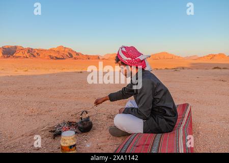 Jordanie - 1er mai 2024 : L'homme bédouin traditionnel infuse du thé sur un feu dans l'immense étendue du désert du Wadi Rum en Jordanie au coucher du soleil Banque D'Images