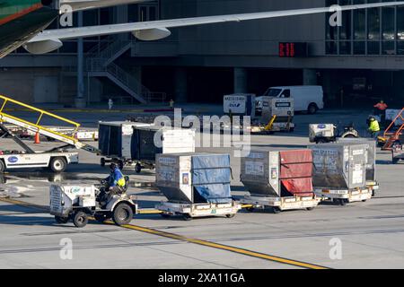 Los Angeles, Californie, États-Unis - 12 janvier 2024 : employé de l'aéroport conduisant un petit tracteur tirant des conteneurs de fret à l'aéroport international de Los Angeles Banque D'Images