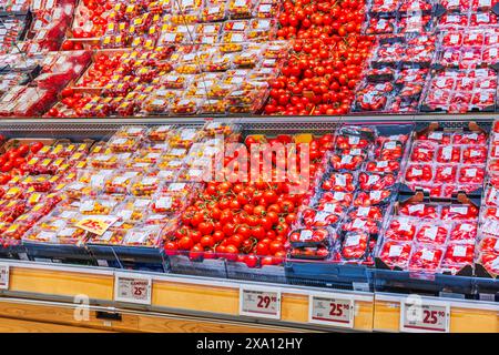 Vue rapprochée des étagères avec différents types de tomates exposées dans la section des légumes d'un supermarché. Banque D'Images