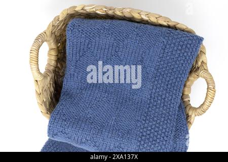 Photographie de table d'une couverture tricotée bleue en motif de tricot arlequin dans un panier sur un fond blanc Banque D'Images