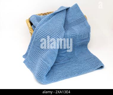 photographie vue de dessus d'une couverture tricotée à la main texturée en laine bleue dans un motif de tricotage géométrique dans un panier isolé sur un fond blanc Banque D'Images