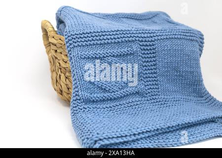 Photographie rapprochée d'une couverture tricotée à la main texturée en laine bleue dans un motif de tricot géométrique dans un panier sur un fond blanc Banque D'Images