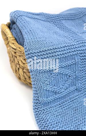 Photographie rapprochée d'une couverture tricotée à la main texturée en laine bleue dans un motif de tricot géométrique dans un panier sur un fond blanc Banque D'Images