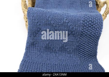 Photographie rapprochée d'une couverture tricotée bleue en motif de tricot arlequin dans un panier sur fond blanc Banque D'Images