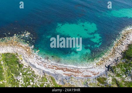 Des eaux bleues claires entourent une île avec des rochers et de l'herbe Banque D'Images