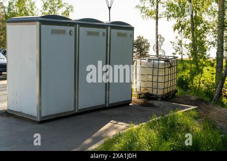 Trois toilettes portatives blanches se tiennent sur une zone pavée dans un cadre de parc Banque D'Images