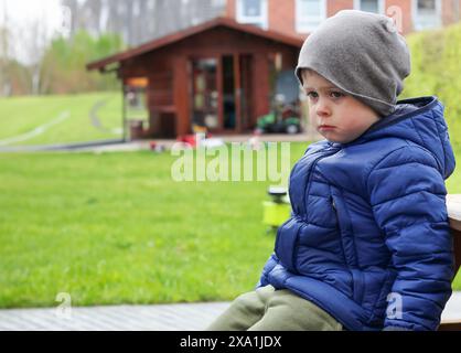 Un mignon petit garçon en bas âge assis triste sur un banc à l'extérieur à Hone Banque D'Images