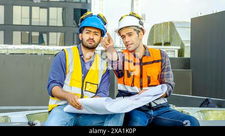 Les ingénieurs discutent des plans sur la construction d'un toit, l'un pointant. Banque D'Images