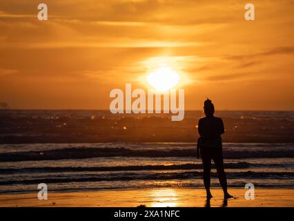 Une silhouette d'une femme debout sur une plage au coucher du soleil Banque D'Images