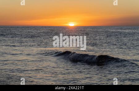 Le soleil se couche sur l'océan, projetant une lueur chaude sur l'eau. Les vagues sont douces, créant une atmosphère paisible Banque D'Images