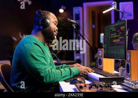 Jeune technicien audio jouant avec des airs de piano sur d'autres chansons, mixant et mastering pour composer une nouvelle bande-son. Producteur qualifié travaille dans le home studio pour créer de la musique. Banque D'Images