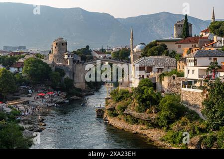 Cette photo capture une rivière qui traverse la ville de Mostar, avec un vieux pont en relief en arrière-plan, en Bosnie-Herzégovine Banque D'Images