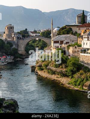 Cette photo capture une rivière qui traverse la ville de Mostar, avec un vieux pont en relief en arrière-plan, en Bosnie-Herzégovine Banque D'Images