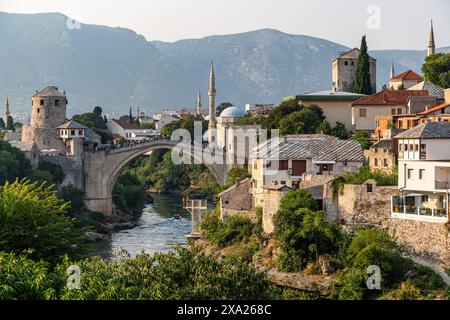 Cette photo capture une rivière qui traverse la ville de Mostar, avec un vieux pont en relief en arrière-plan, en Bosnie-Herzégovine Banque D'Images