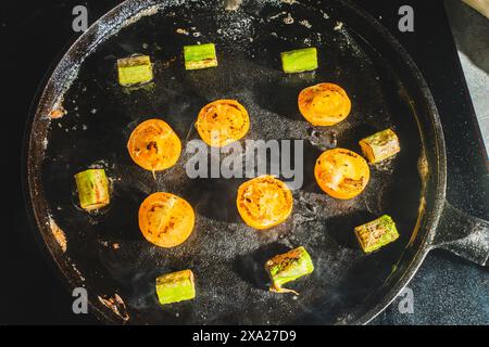 Les tomates cerises et les asperges sont frites dans une poêle en fonte. Gros plan. Photo de haute qualité Banque D'Images