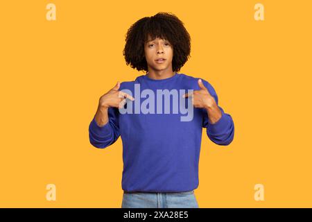 Jeune homme en Blue Pullover pointant vers lui-même contre Yellow Banque D'Images
